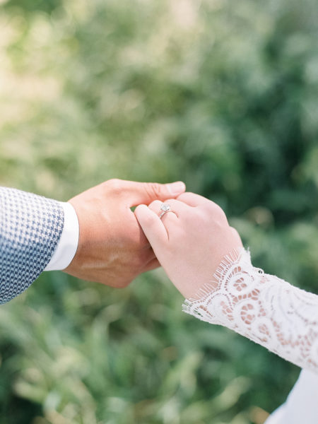 Close up of a mixed race wedding couple holding hands over a field of grass.